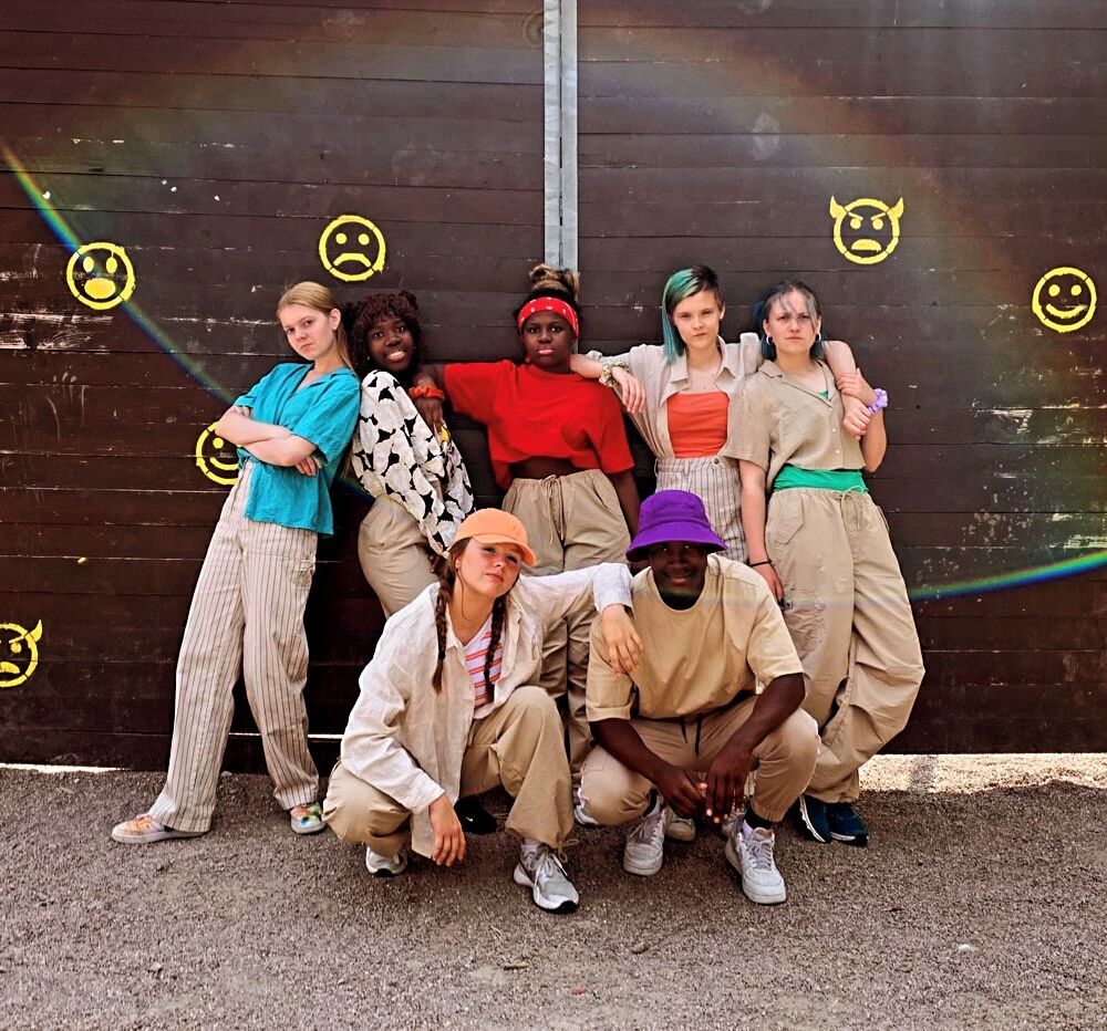 en grupp dansare gör poser mot en vägg med smileys.