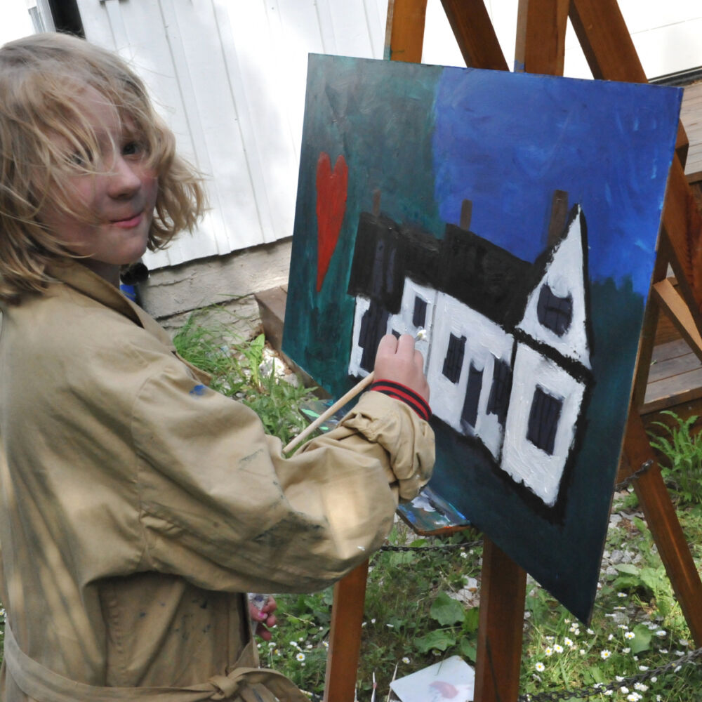 ett barn med ljus hår som målar framför stafflin