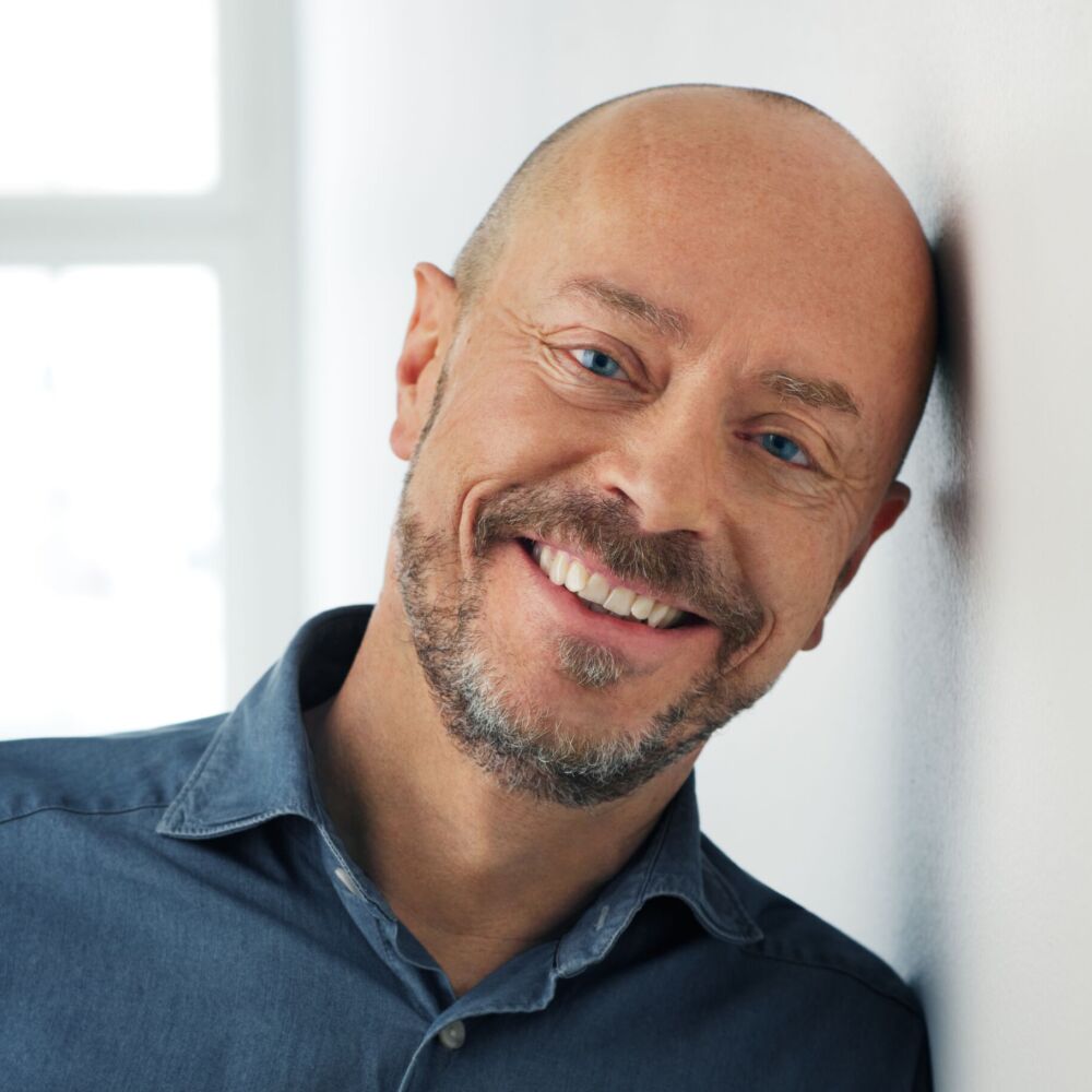 en man i en blå skjorta lutar sig mot väggen