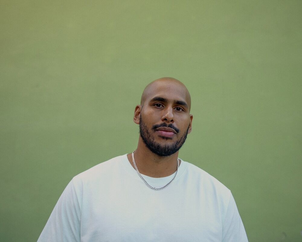 en svart man i en vit T-shirt framför en grön vägg