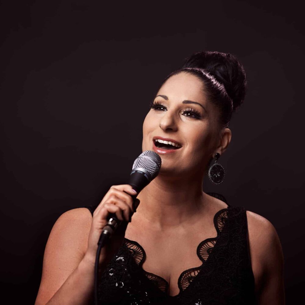 sångerska i en svart klänning och med brun hår sjunger i mkrofon