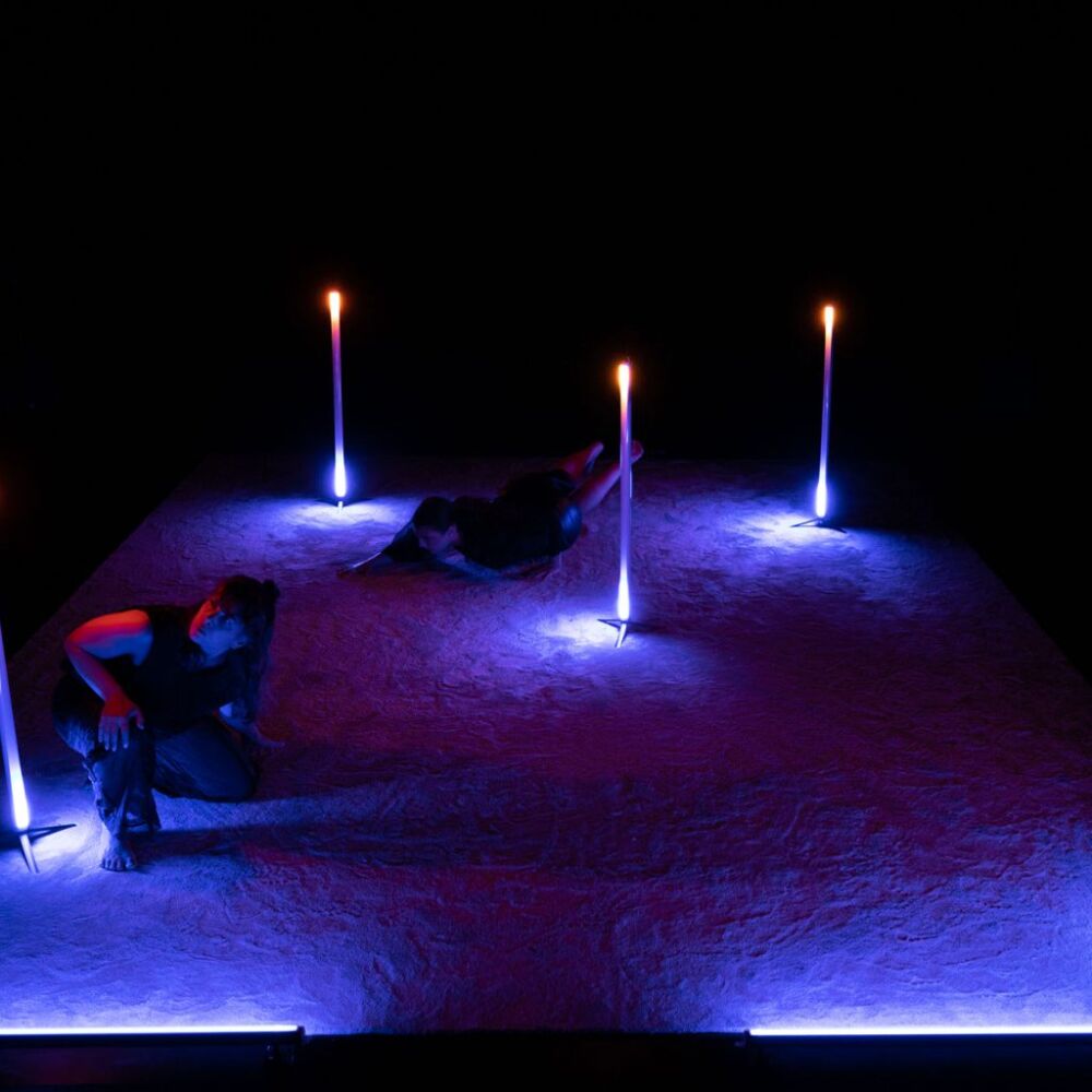 tre dansare i ett mörkt rum dansar med tre neonlampor