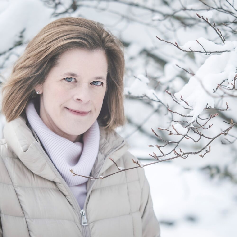 en kvinna i en vit jacka med ljust hår mot snöigt bakgrund