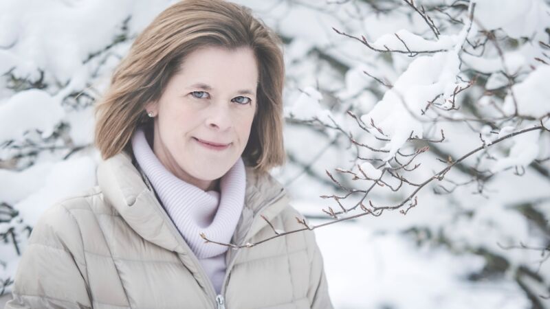 en kvinna i en vit jacka med ljust hår mot snöigt bakgrund