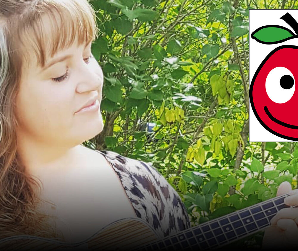 en kvinna med lång hår spelar guitar, med en grön buske bakom. På bildenvisas också en ritat äpple med ögon