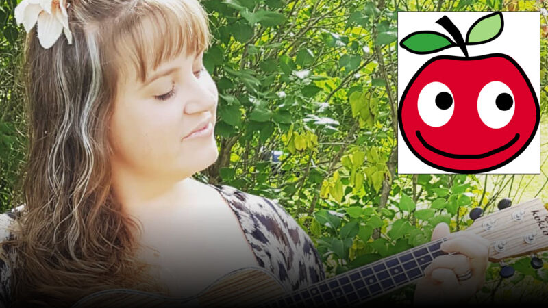 en kvinna med lång hår spelar guitar, med en grön buske bakom. På bildenvisas också en ritat äpple med ögon