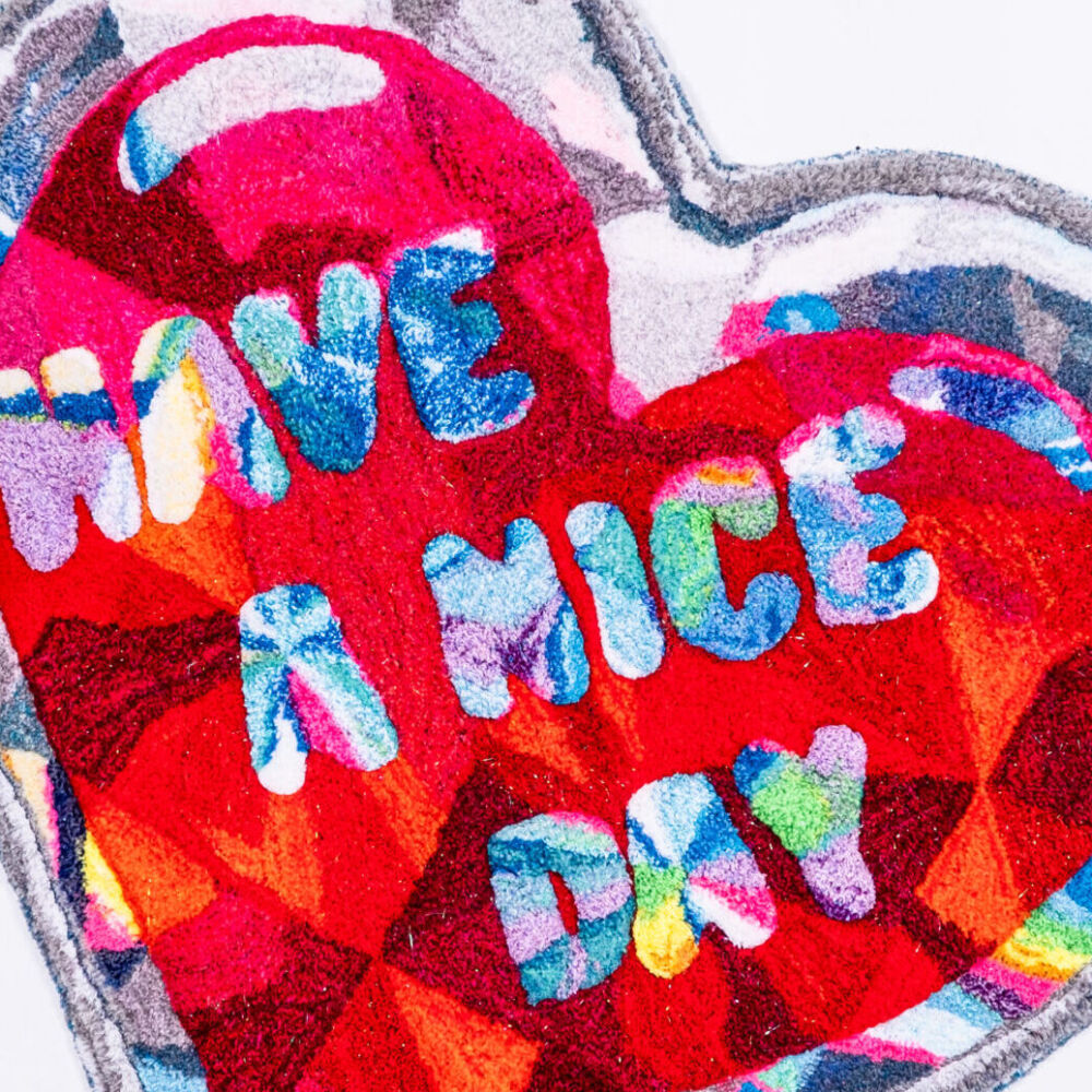 Ett konstverk i tyg upphängt på väggen format som ett hjärta med texten Have a nice day