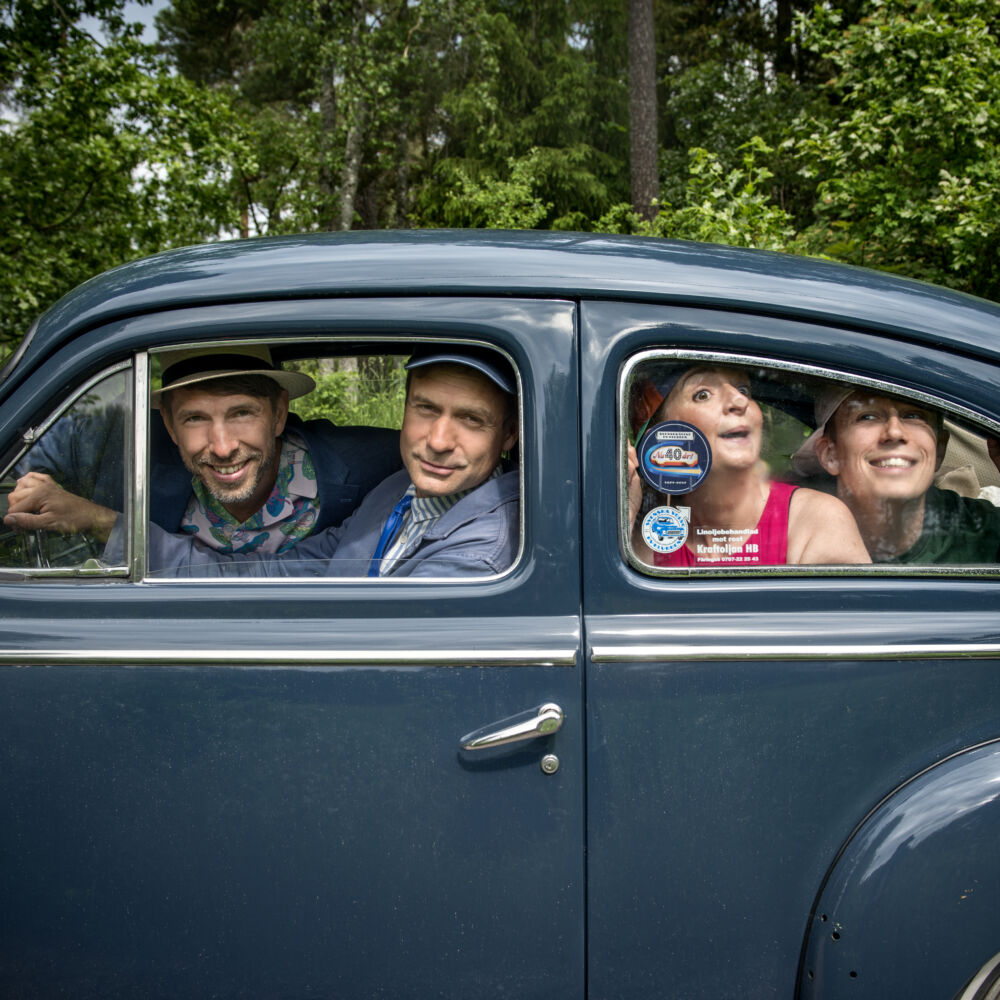 en kvinna och tre män sitter i en blå bil