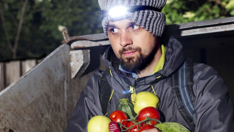 en man i en grå mössa och pannlampa håller grönsaker medan han kliver ur ut container