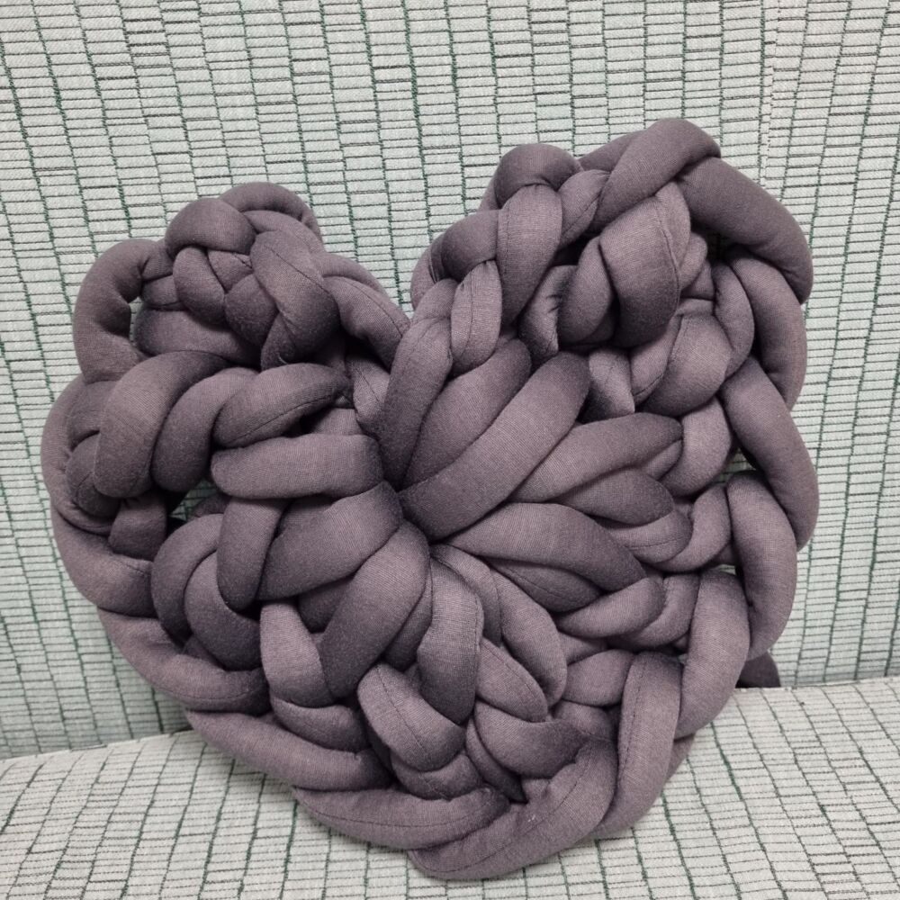 en grå virkade hjärta ligger på en grön fåtölj