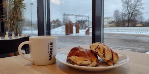 Kaffekopp och en bulle på fat vid ett fönster