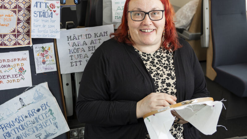 en kvinna i en svart tröja och med röd hår sitter och broderar