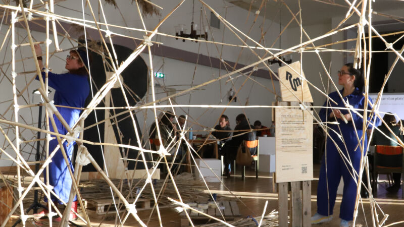 två artister skapar en skulptur av pinnar inne i museum