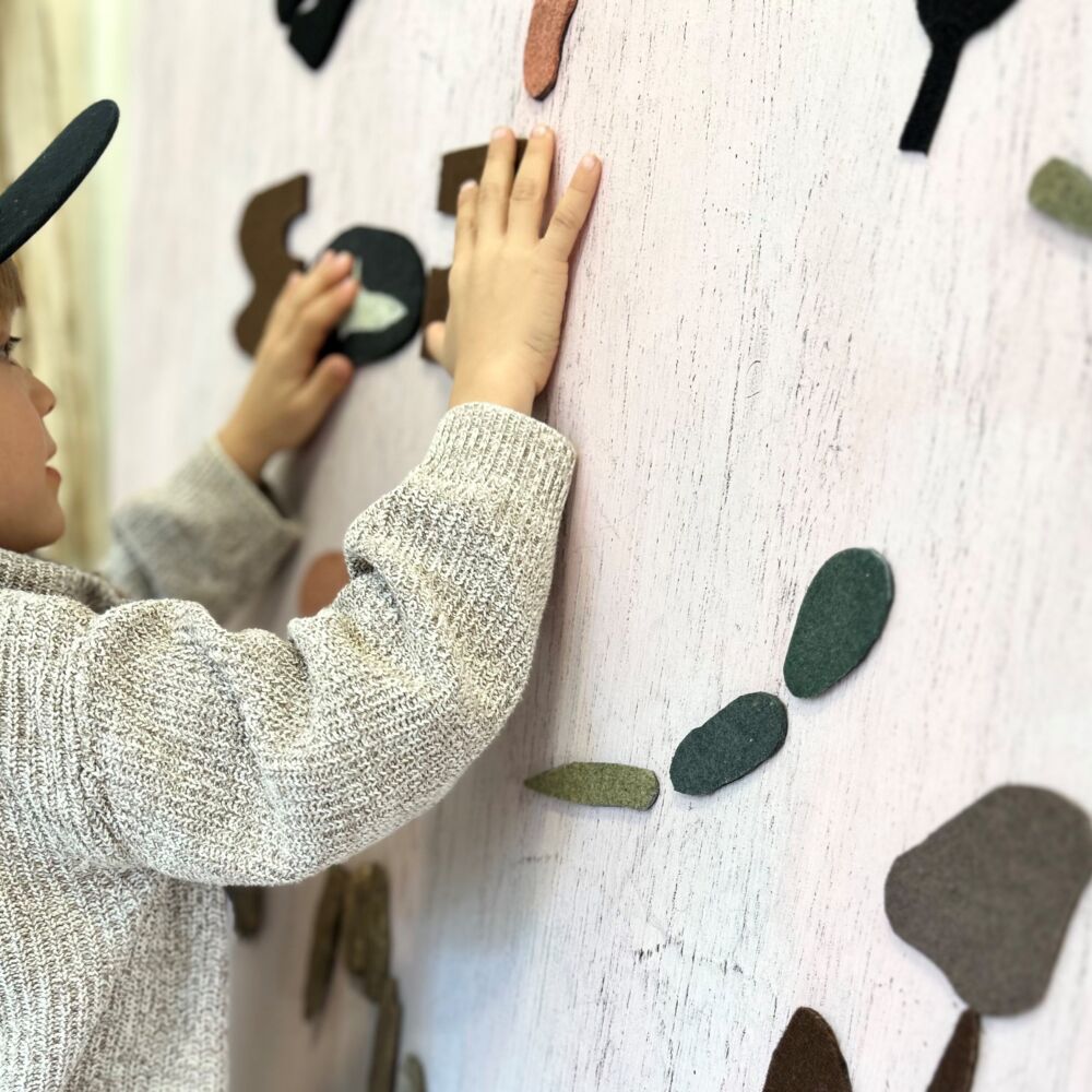 En liten pojke i en svart keps känner på filtkonstverk på väggen