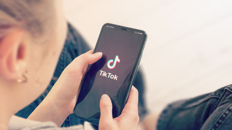 en tjej håller mobilen i handen med appen tiktok på skärmen som syns