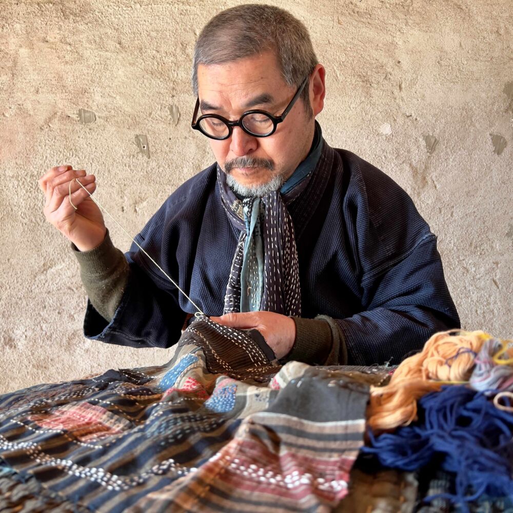 Takao Momiyama sitter vid ett bord och syr.