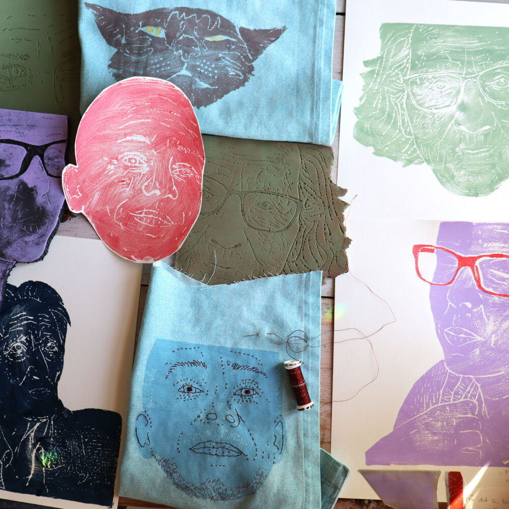 Ett bord med papper på. papperna är målade i blått, lila och rött. På papprena är ansikten tryckta.