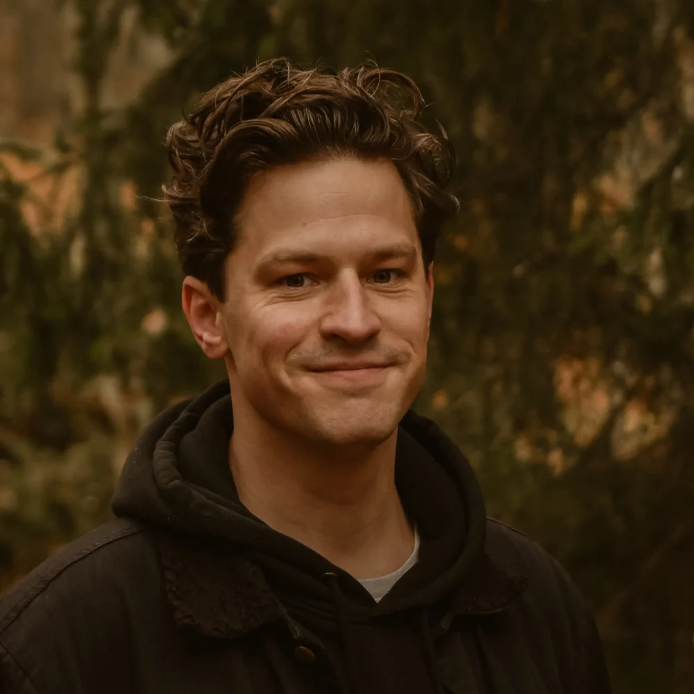 Henrik Wahlström författare, konstnär och föreläsare. Han har lockigt hår . Han står ute och har skog i bakgrunden.