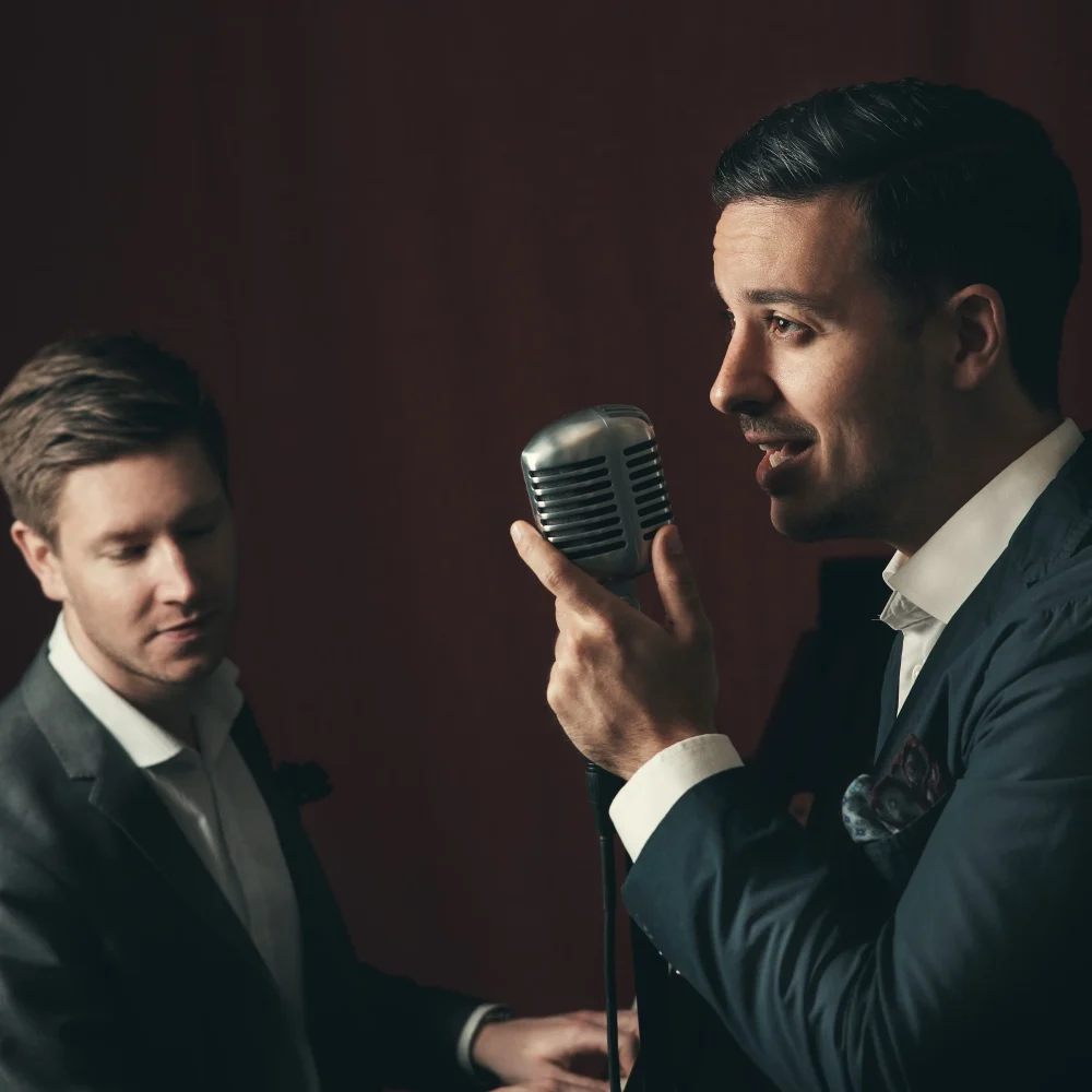 Två män i kostym , den ena sjunger i en mikrofon