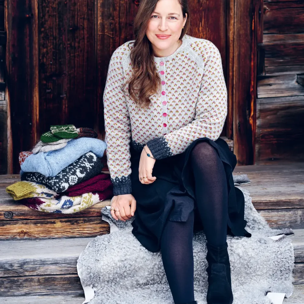 Maja Karlsson, författare sitter på en trätrappa med beige kofta, kjol och långt hår.