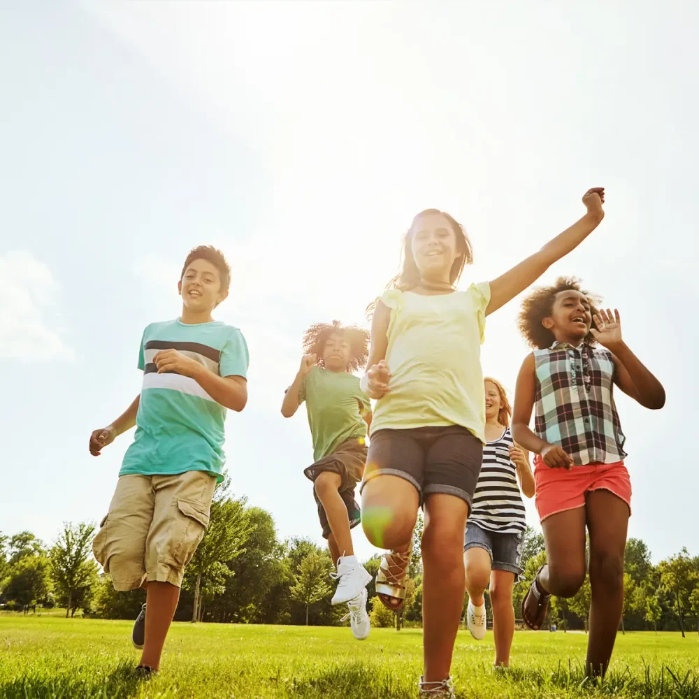 glada barn springer på en gräsmatta i solen.