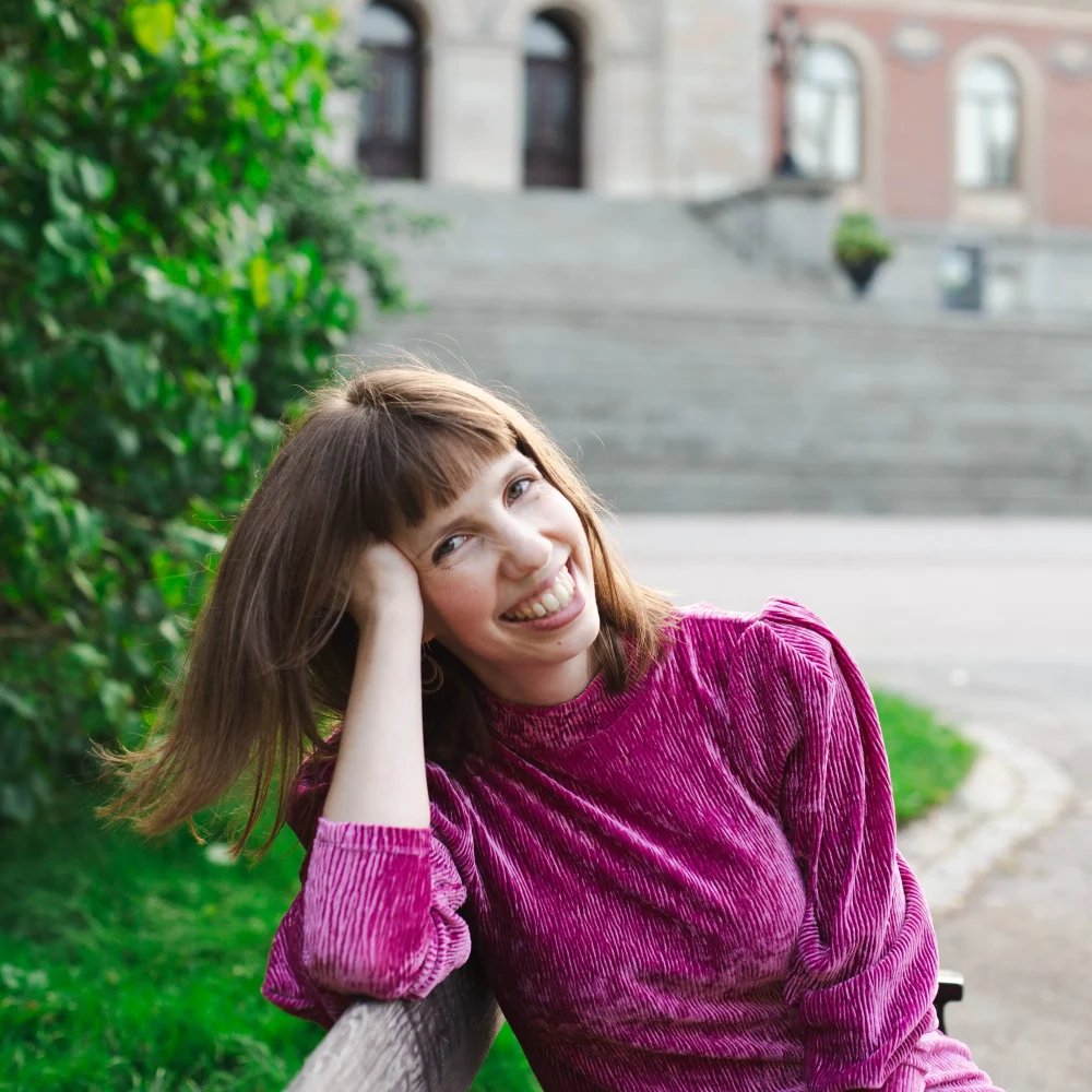 Kvinna ute i en park med lila tröja . Hon heter Anna Ahlund och är författare