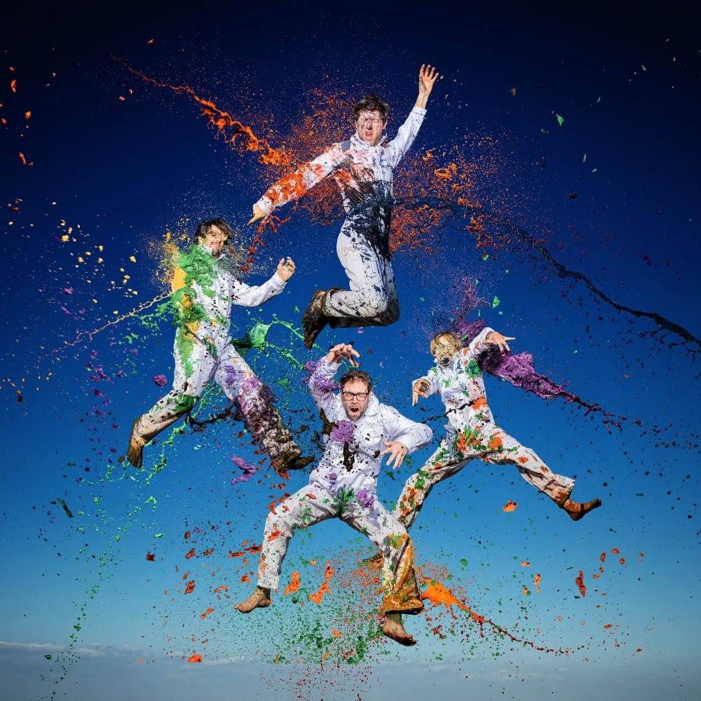 Fyra personer hoppar och det skvätter färg på dem.