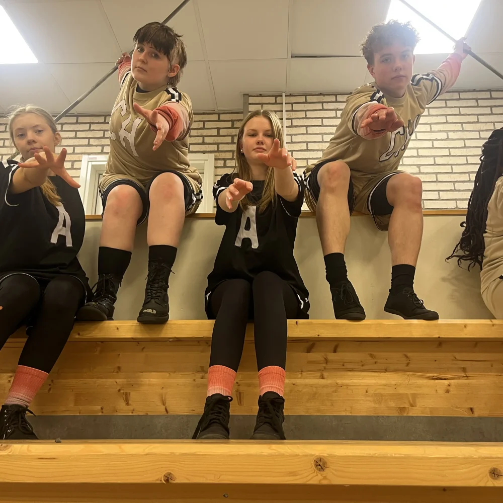 Sex ungdomar sitter på en bänk och sträcker sina händer mot kameran