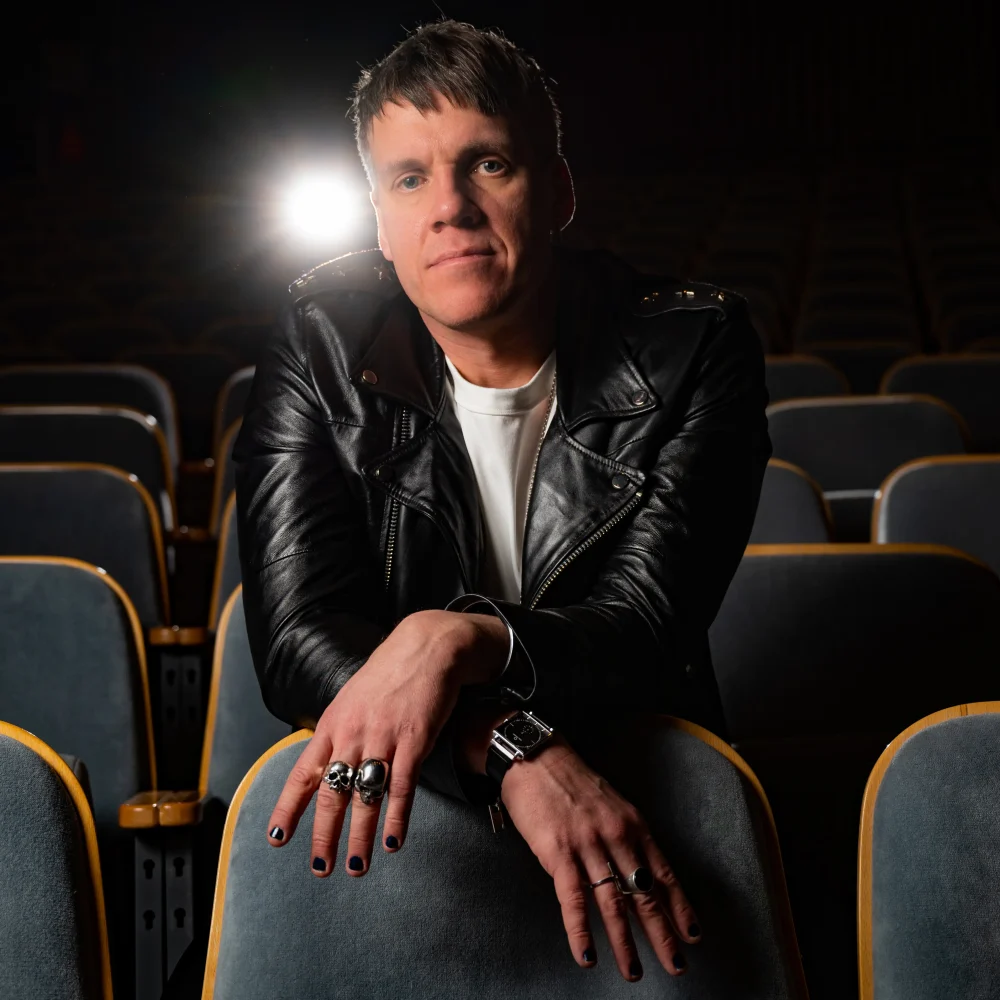 Bild på en ung man som heter Ismael Ataria som sitter med skinnjacka och vit t-shirt och tittar in i kameran