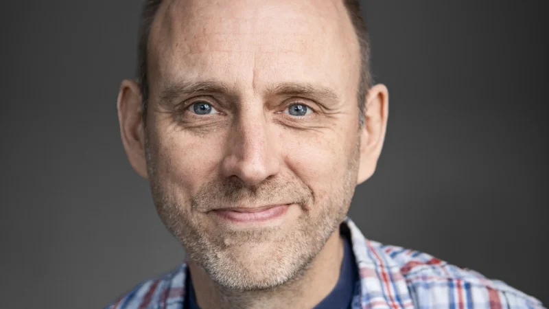 Linus Nyman författare sitter med handen mot kinden och har en rutig skjorta på sig.