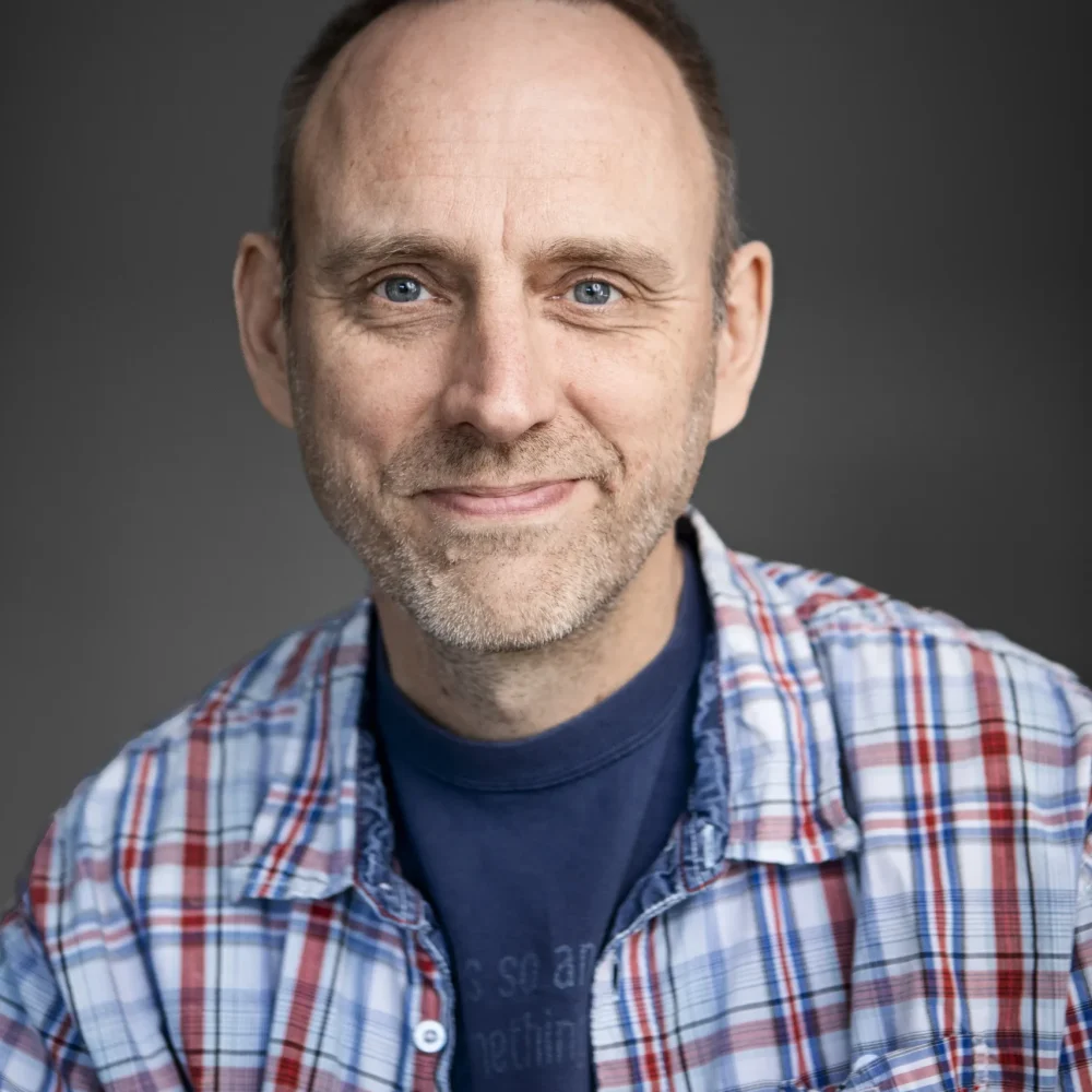 Linus Nyman författare sitter med handen mot kinden och har en rutig skjorta på sig.