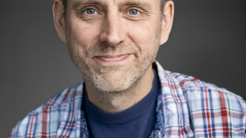 Linus Nyman författare sitter med handen mot kinden och har en rutig skjorta på sig.