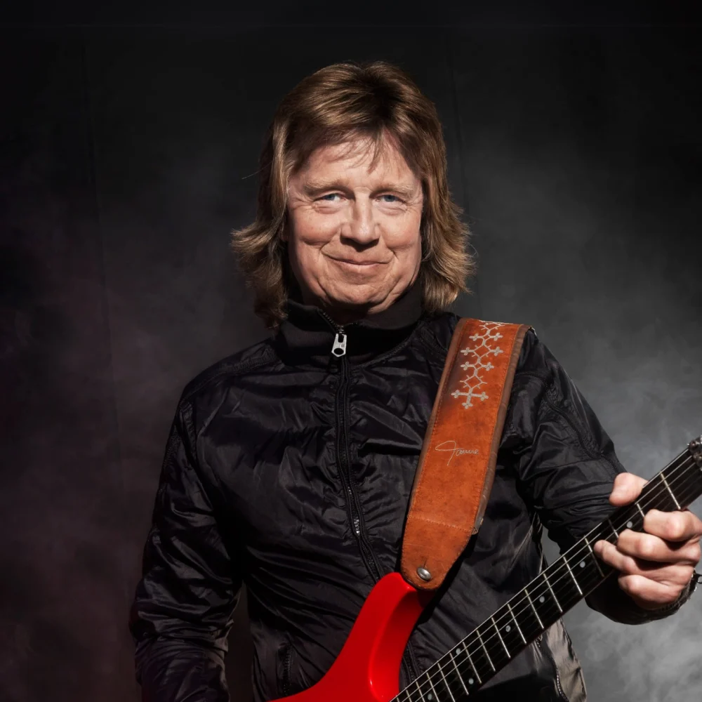 Gitarrisetn Janne Schaffer. Står med sin gitarr och ler , har långt hår.