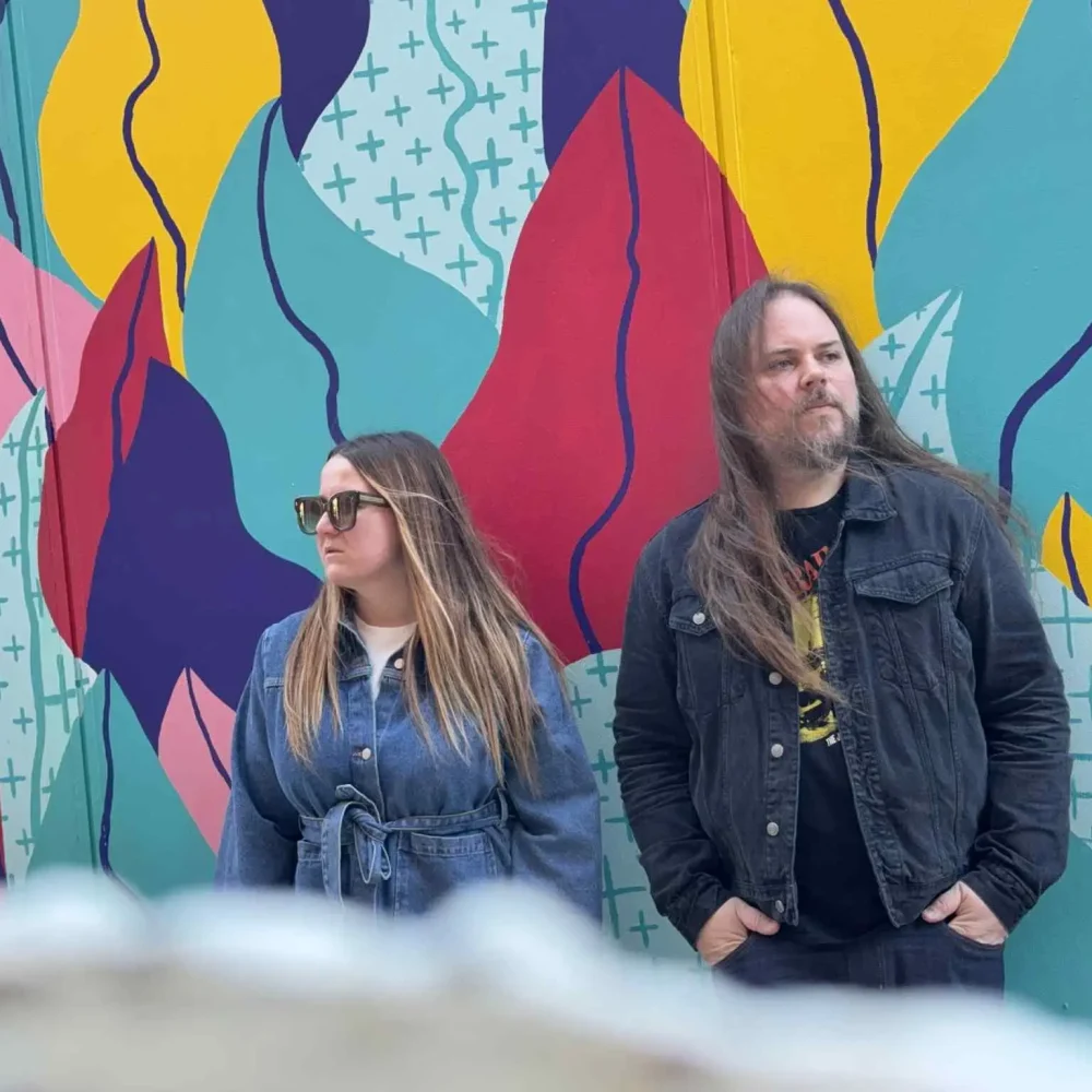 Färglad bakgrund med en kvinna och en man framför med solglasögon. De är artister i bandet River talks