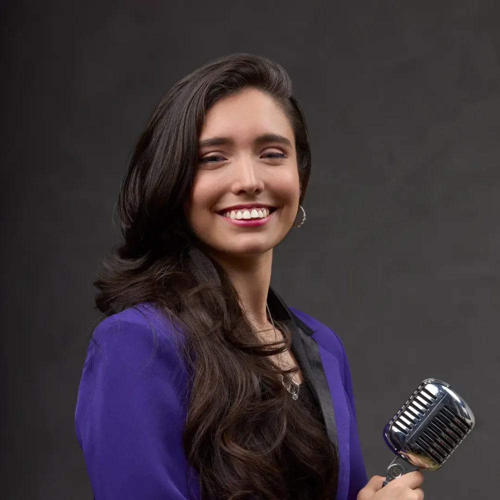 Artisten Milagros Amud. Kvinna mörkt långt hår och lila kavarj ,Glad med mikrofon