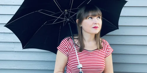 Tjej med rött läppstift och röd-randig tröja som står med ett svart paraply. Hon heter Linnea Ingemarsson