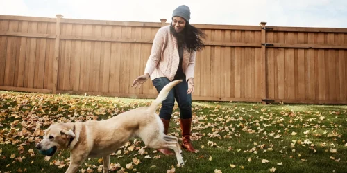 en kvinna i en mössa och ljuströja leker med en hund i trädgården